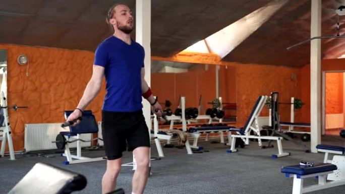 在一个废弃的工厂硬核健身房里，运动赤膊健美男子用跳绳锻炼。他在激烈的交叉健身训练中浑身是汗。