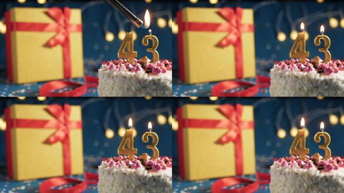 白色生日蛋糕编号43点灯燃烧的金色蜡烛，带灯的蓝色背景和用红丝带绑起来的礼物黄色盒子。特写