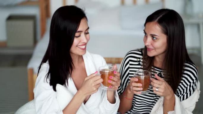 两个年轻漂亮的女人在家里说话，微笑和喝茶