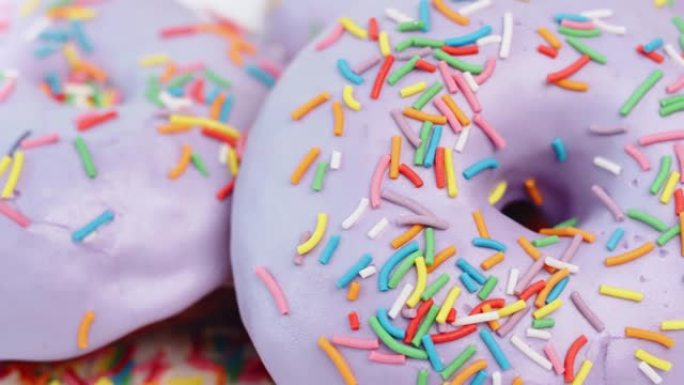 极端特写旋转的彩色糖果覆盖着紫色的糖衣甜甜圈戒指。4k龙红相机