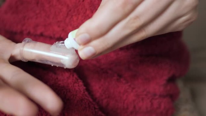 女性手在按摩器牙刷上涂抹口香糖凝胶。出牙概念。慢动作和特写