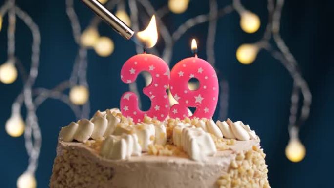 蓝色背景上有39号粉色蜡烛的生日蛋糕。蜡烛着火了。慢动作和特写视图