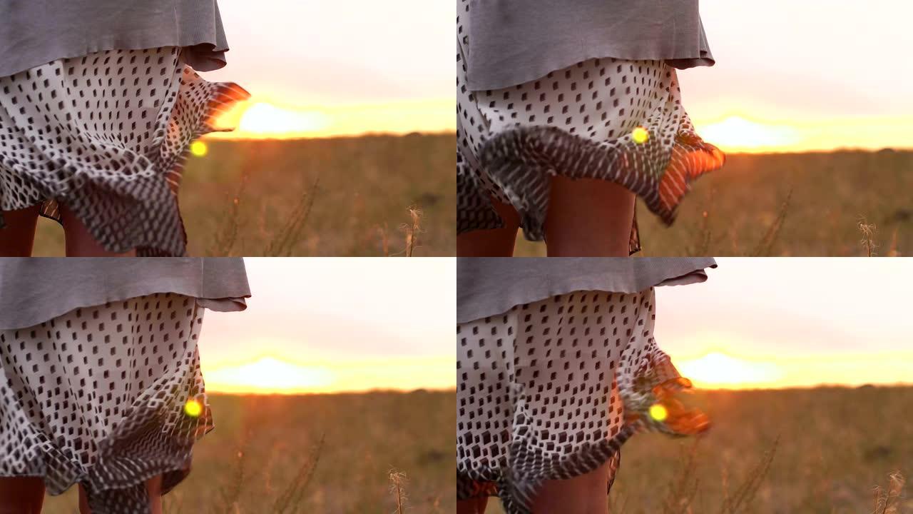 日落时站在野外，穿着裙子在风中飘扬的女孩的特写镜头。