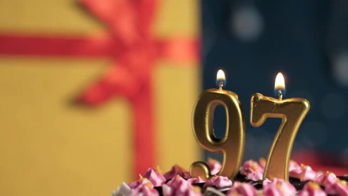 生日蛋糕97号点火器燃烧的金色蜡烛，蓝色背景礼物黄色盒子用红丝带绑起来。特写和慢动作