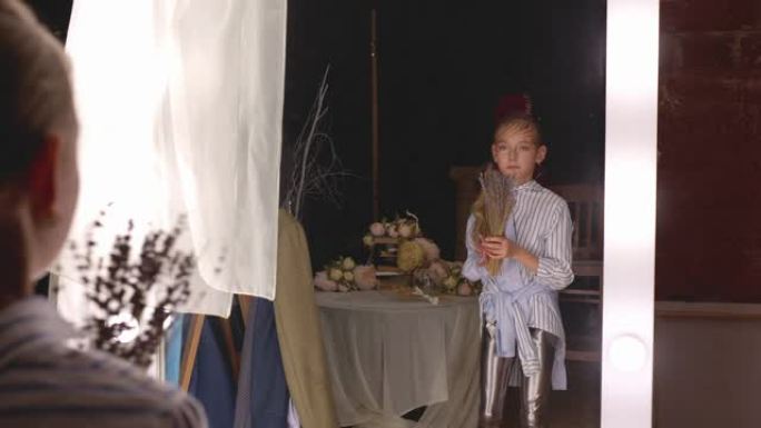 年轻女孩女演员在更衣室用花束前镜排练。少女少年在更衣室前照明镜中与花束共舞。
