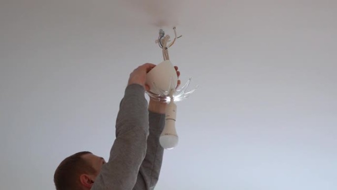 修理和家庭装饰。一个人从天花板上把一盏灯挂在房间里。