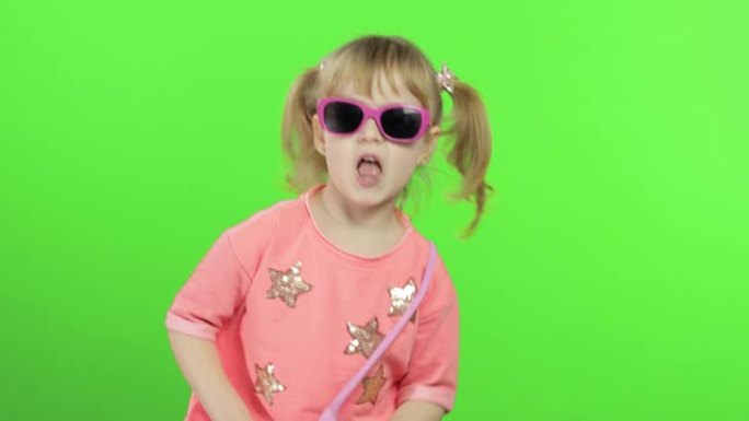 穿着粉色衬衫和太阳镜的积极女孩跳舞和摆姿势。色度键