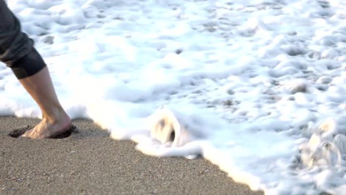 女性赤脚在海边的沙滩上行走，海水冲走了脚印