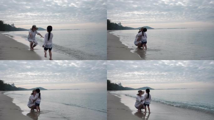 暑假快乐的亚洲家庭，女儿早上在海滩上抱着母亲跑，日出。假日和旅游概念。慢动作