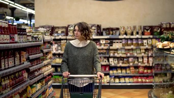 一个波浪形的女人的肖像，穿着休闲的衣服，正开着购物车穿过超市里满是货架的那排，环顾四周。漂亮女孩，日