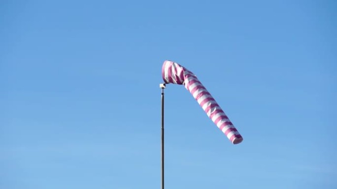 带有红色和白色条纹的风向袋显示了风的方向和速度。锥风指示器在蓝天背景上发展。Weathersock是