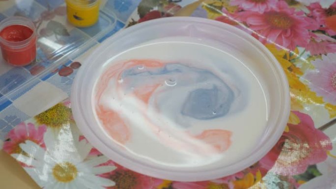 在液体中混合油漆。儿童认知实验。刷子上的一滴油漆掉入白色液体中。