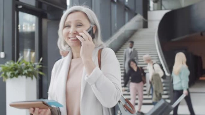 快乐的混血女士与登机牌在机场通过电话聊天