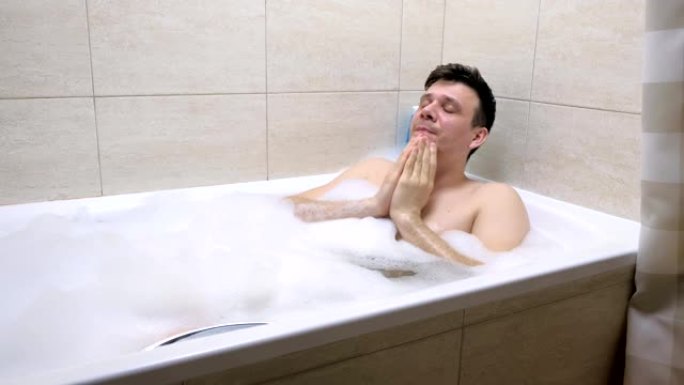 一个成年男子坐在浴室里，用泡沫擦脸。