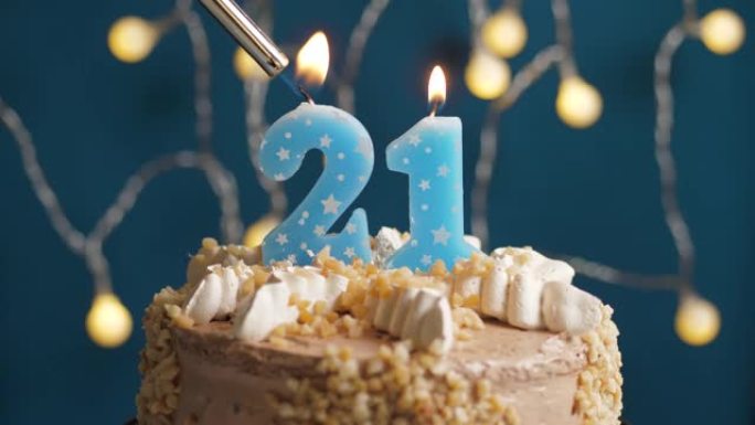蓝色背景上有21号蜡烛的生日蛋糕。蜡烛着火了。慢动作和特写视图