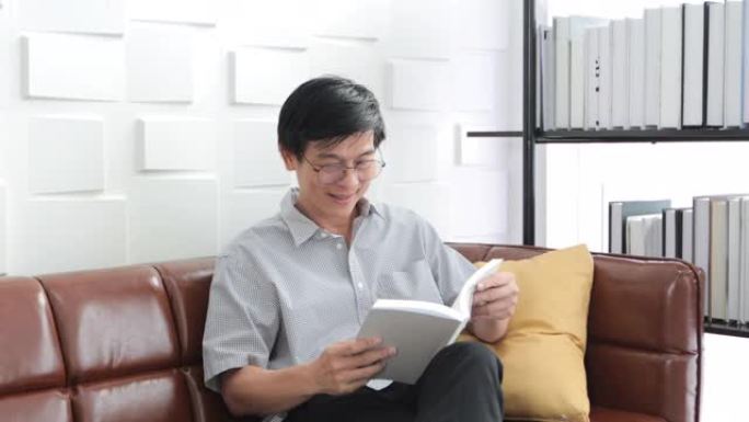 亚洲老人在家客厅沙发上看书，亚洲老人与阅读杂志一起放松和快乐