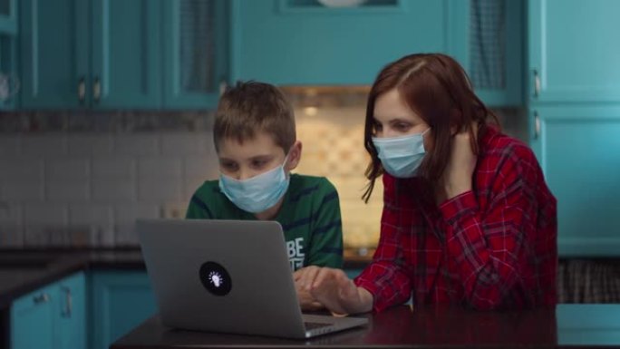30多岁的母亲和男孩戴着医用口罩看着笔记本电脑屏幕，与亲戚在线交谈，挥手致意。家庭在医疗口罩在家里的
