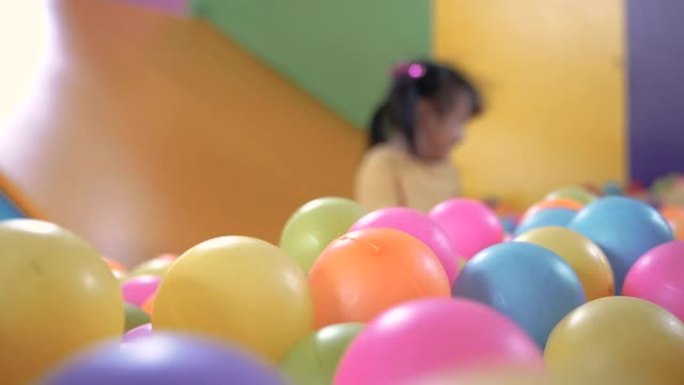 可爱的小女孩在室内儿童游乐场里玩塑料干水池里的滑梯，里面有五颜六色的球。