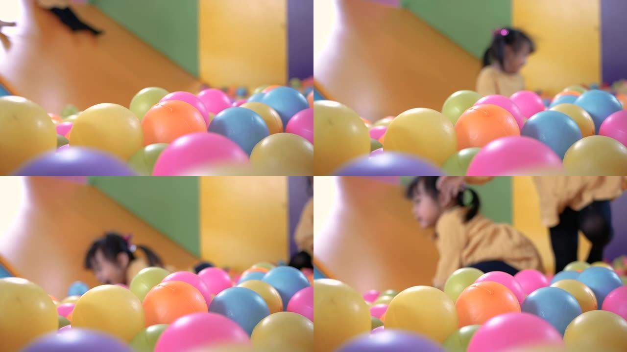 可爱的小女孩在室内儿童游乐场里玩塑料干水池里的滑梯，里面有五颜六色的球。