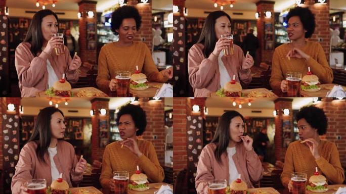 两名成年女性在酒吧享用啤酒和汉堡