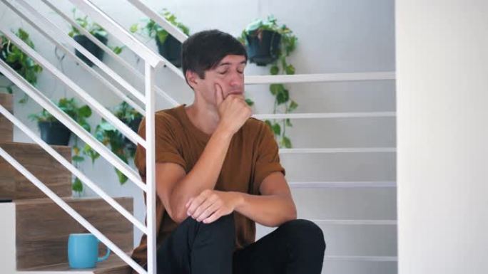 沉思的悲伤和沮丧的年轻人独自坐在家里的楼梯上: 痛苦的悲伤的人。
