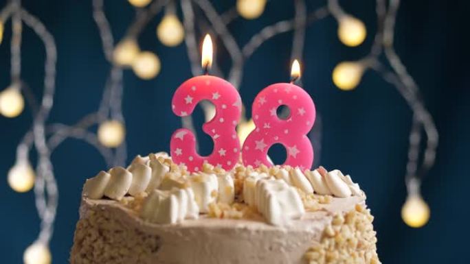 蓝色背景上有38号粉色蜡烛的生日蛋糕。蜡烛吹灭了。慢动作和特写视图