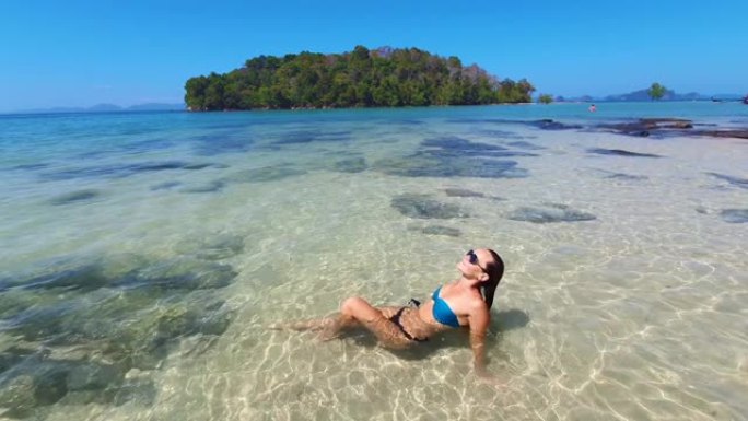 热带概念视频。棕色皮肤的年轻女子躺在岛屿背景的海浪上。