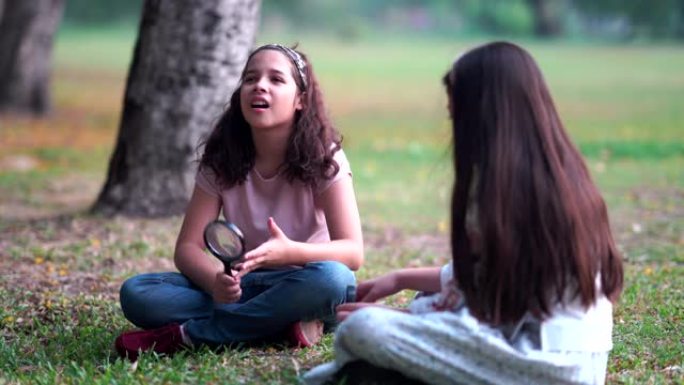 两个漂亮的年轻女孩和朋友一起通过放大镜看着植物上的昆虫，在公园里玩耍，公园里阳光明媚的秋天，在公园里