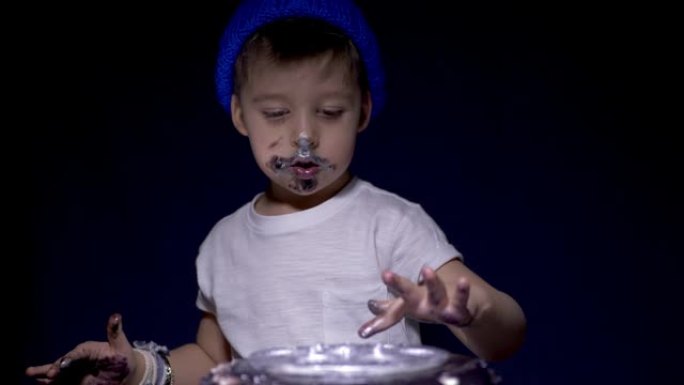 戴着蓝色帽子和白色t恤的男孩吃节日的黑色蛋糕