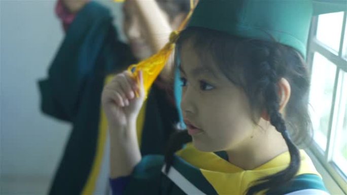 站在学校里，戴着毕业帽和礼服的亚洲小学女孩微笑。