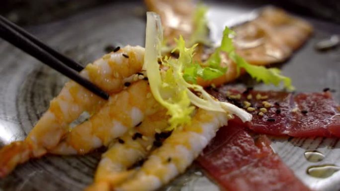 美味的日本餐厅，用筷子吃海鲜的人。在灰色盘子上放鲑鱼和金枪鱼鱼片，配以绿色沙拉和香料，用橄榄油轻轻炸