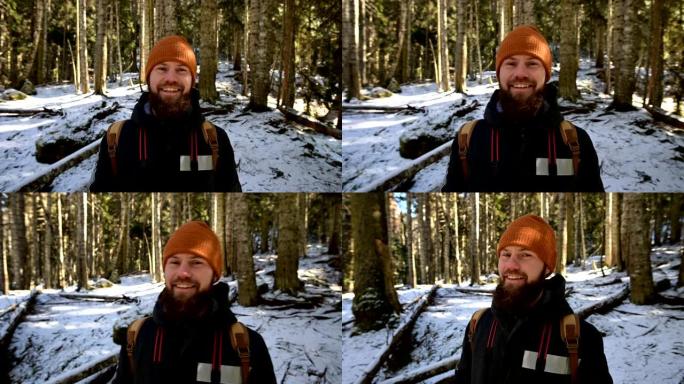 一个快乐的大胡子笑着的年轻人的肖像，他的背包站在针叶树的冬季森林中
