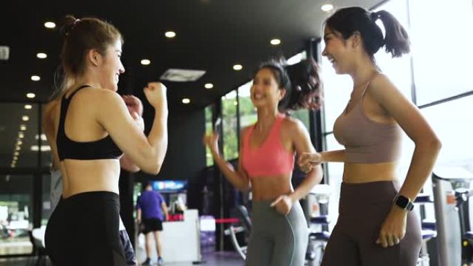 微笑男人和女人在健身馆里手拉手。一群年轻人在锻炼后在健身房做高五手势。训练后快乐成功的锻炼课。团队合