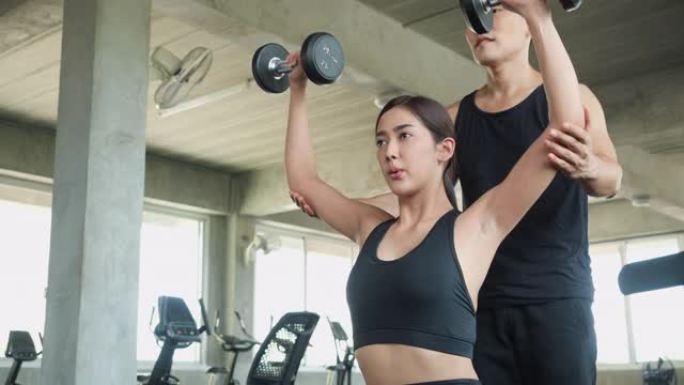 运动的男人和女人玩哑铃练习，进行手臂耐力训练，以增强和调理肩部肌肉。重量训练、运动和健康教育的概念。