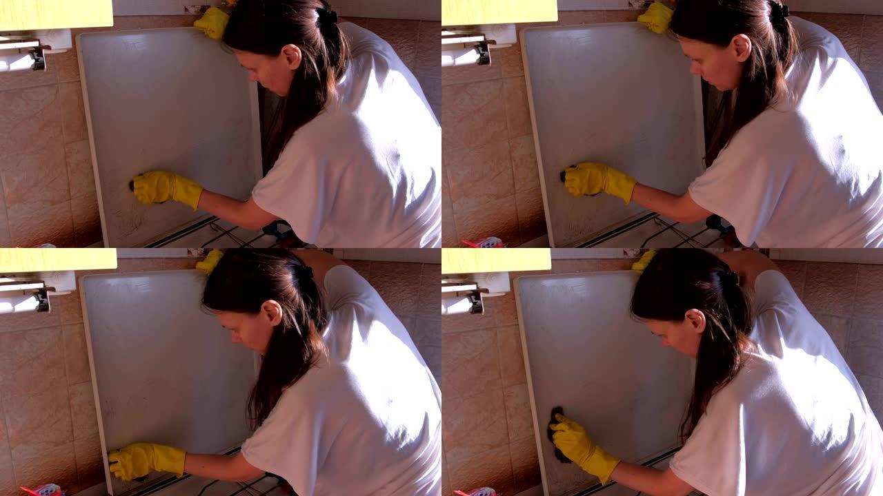 穿着黄色橡胶手套的女人在厨房洗脏煤气炉金属海绵。