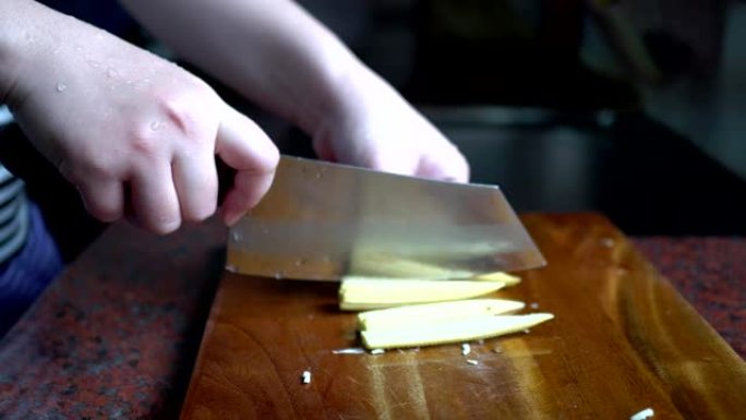 妈妈用菜刀在厨房的砧板上切小玉米。