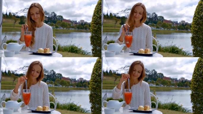 女孩在咖啡馆用勺子搅拌冷橙色饮料