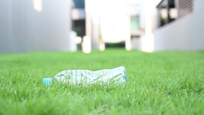 志愿者的4k近距离手从公园的草地上捡起一个塑料瓶。零浪费和停止使用塑料概念的想法背景。