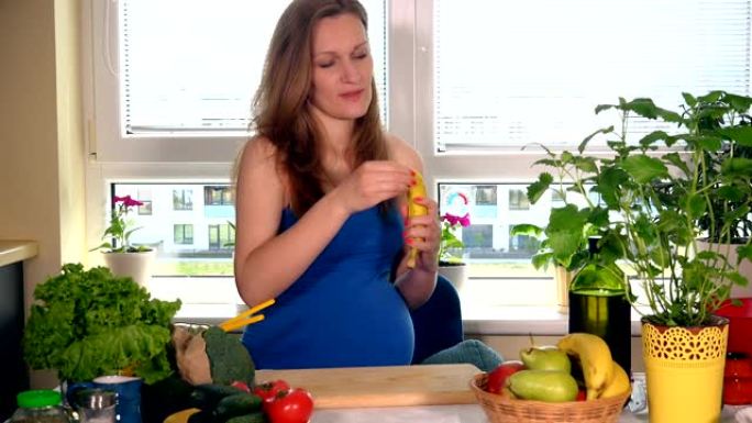 饥饿微笑的大肚子孕妇在厨房剥香蕉