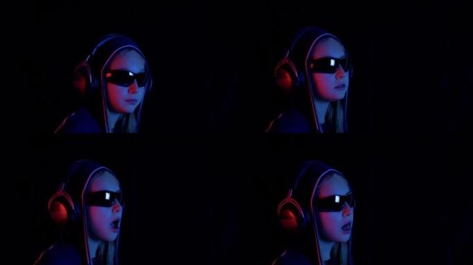 戴兜帽和黑色太阳镜的少女在黑暗的房间里听耳机音乐，红色和蓝色照明。肖像少女嚼口香糖，在霓虹灯的黑色房