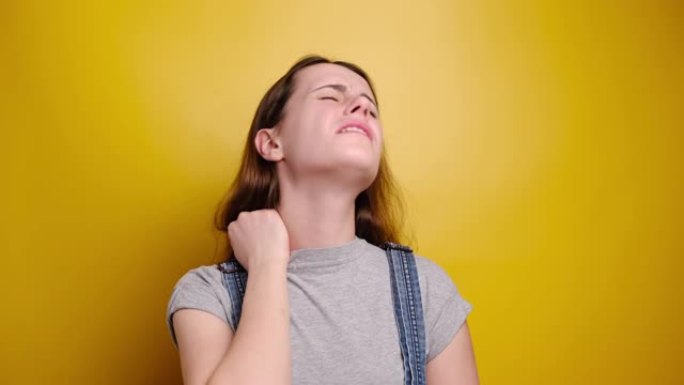 疲惫心烦的年轻女子感到僵硬疼痛颈部疼痛概念摩擦按摩紧张的肌肉患有纤维肌痛，表情阴郁，孤立在黄色背景上