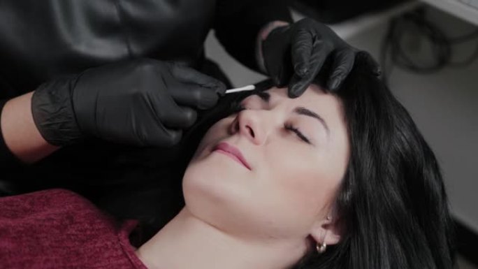 专业永久化妆师在客户的眉毛上涂抹麻醉剂