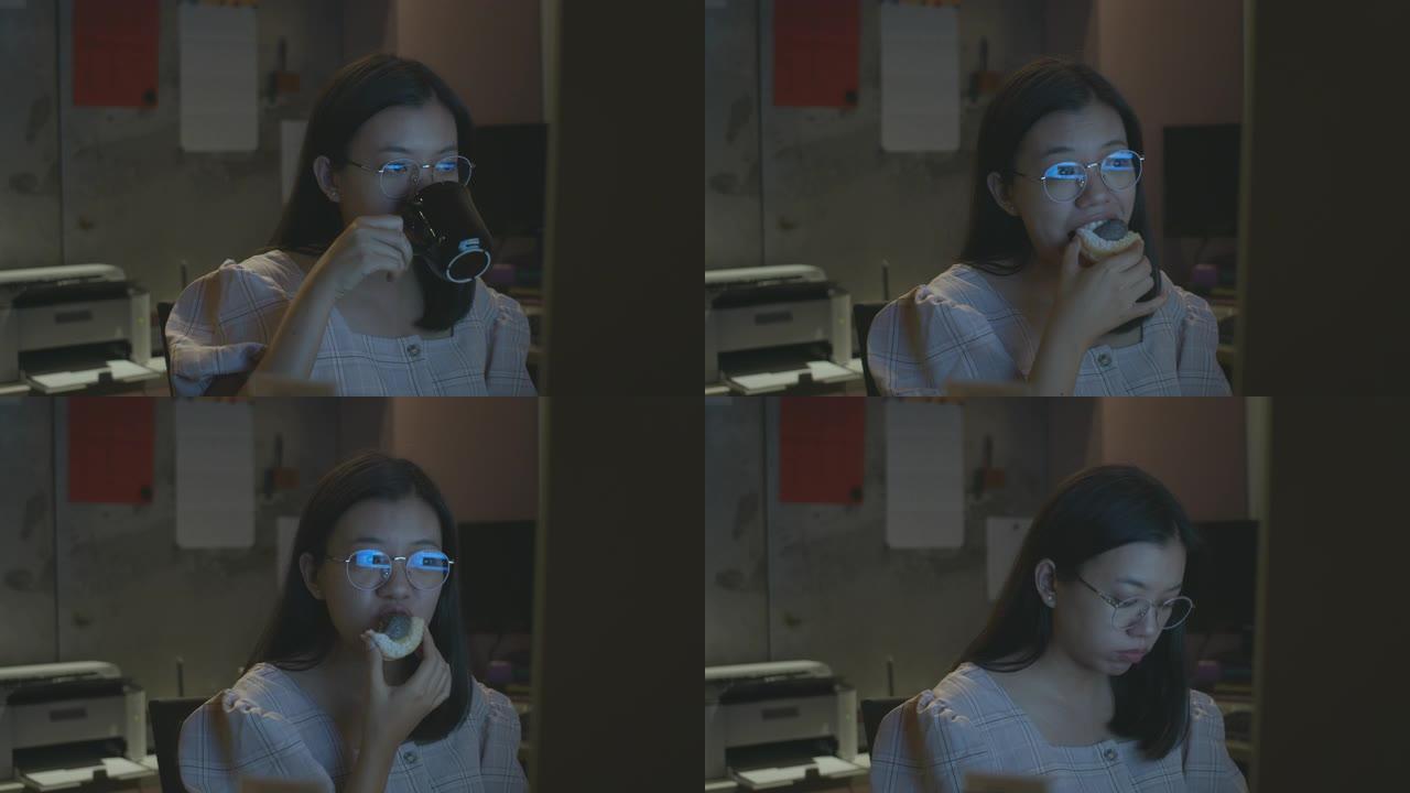 亚洲美女在办公室背景下晚上在电脑屏幕上工作和吃饭，眼镜反射。加班到深夜的概念。