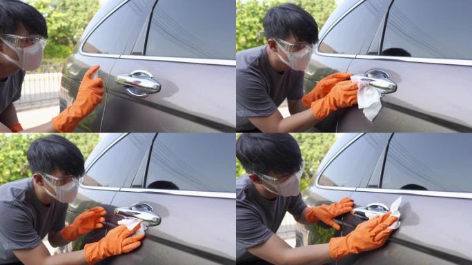 一个戴着安全眼镜和面罩的男人，戴着手手套擦拭汽车清洁新型冠状病毒肺炎病毒的门把手表面。