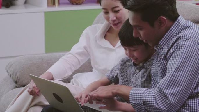 亚洲家庭父母和儿子使用笔记本电脑申请申请观看家庭娱乐。霍利迪家庭度假与家庭技术