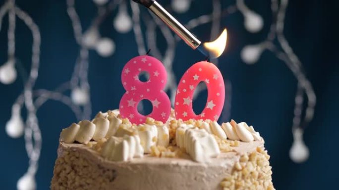 蓝色背景上有80号粉色蜡烛的生日蛋糕。蜡烛着火了。慢动作和特写视图