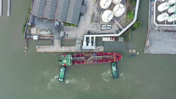 空中俯视图拖船将油轮推到装货码头，以从炼油厂装载或卸载石油，以进行运输或能源概念背景。