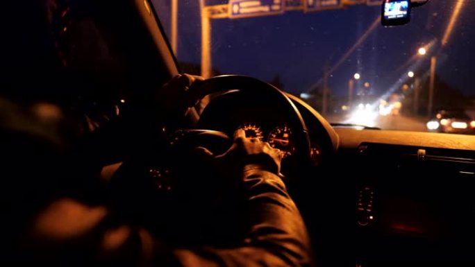 近距离的男性双手握住方向盘，并在夜间在高速公路上自动驾驶。司机开着他的越野车在路上行驶。年轻人晚上开