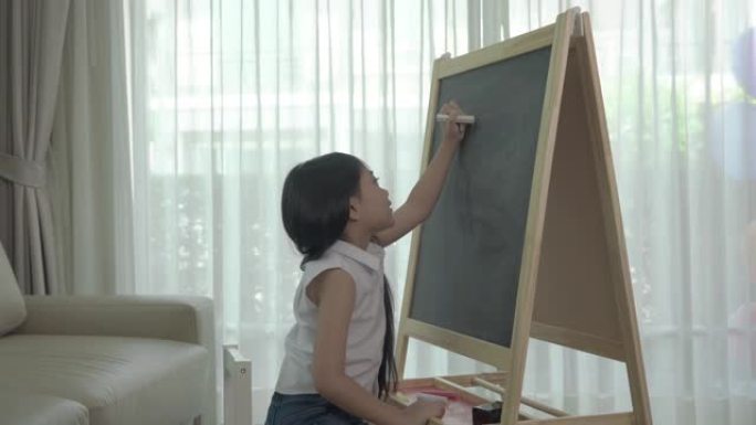 亚洲女孩在家里客厅的桌子上用彩色粉笔在黑板上写英语字母。父母身份或爱和结合的表达概念。