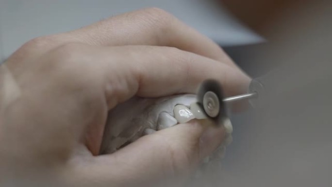 牙科技师拿着带有牙齿的人造颚模，并在实验室中对其进行抛光。牙医用专业工作工具刷牙